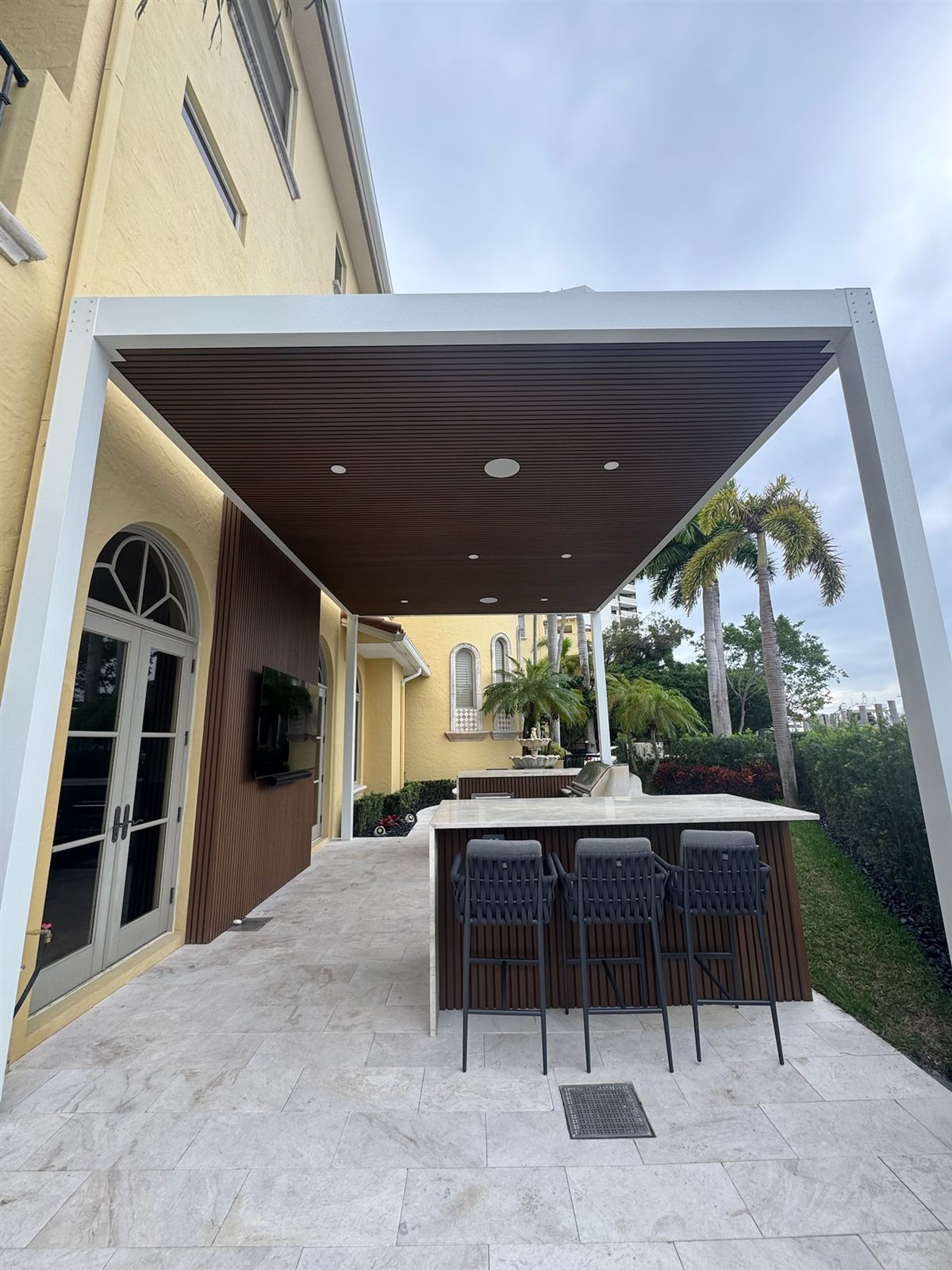 Open Sky custom PVC roof pergola with fluted-wood ceiling over an outdoor kitchen and bar